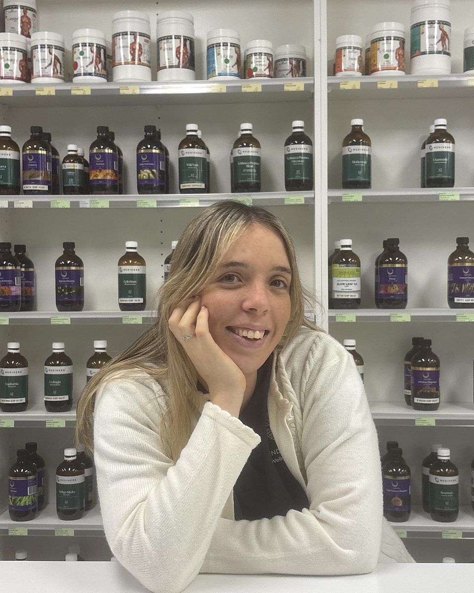 Brooke smiling, leaning on the dispensary counter in front of shelves of herbal extracts